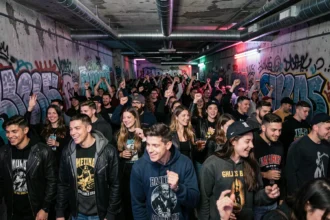 Dancefloor animé d'une boite électro souterraine à Paris avec une foule de jeunes adultes dansant sous des néons UV sur fond de murs en béton brut