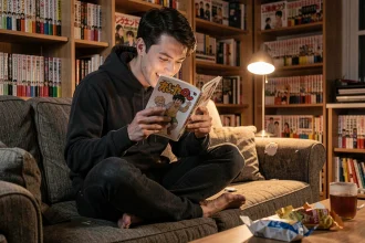 Jeune homme lisant un manga Black Clover sur un canapé dans un appartement cosy le soir