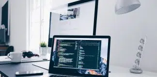 A MacBook with lines of code on its screen on a busy desk