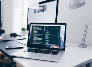 A MacBook with lines of code on its screen on a busy desk